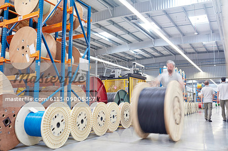 Male worker rolling large spool in fiber optics factory