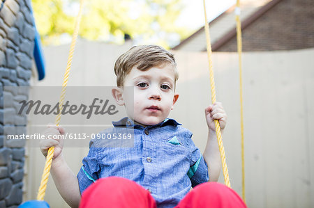 Portrait serious preschool boy swinging on swing