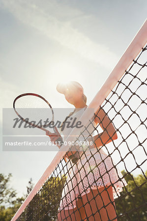 Focused female tennis player with tennis racket standing at net on sunny tennis court