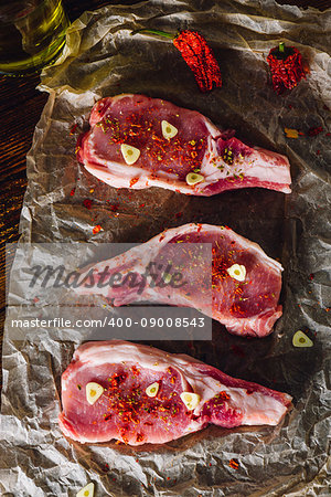 Three Raw Pork Steaks with Spices on Parchment Paper. Vertical.