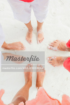 Top view image of feet of family standing on the white sand beach.