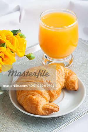 Morning breakfast with croissant and orange juice in glass, yellow roses  on vintage silver tray.
