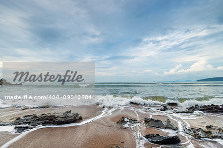 Sharp stones and sea foam on the sandy shore of Thailand