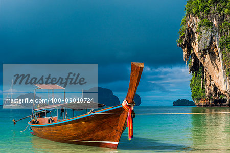 A Thai boat with a long tail near the shore, a blue rain cloud over the Andaman Sea