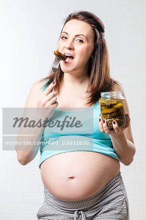 Hungry pregnant woman with a jar of pickled cucumbers against a brick wall background