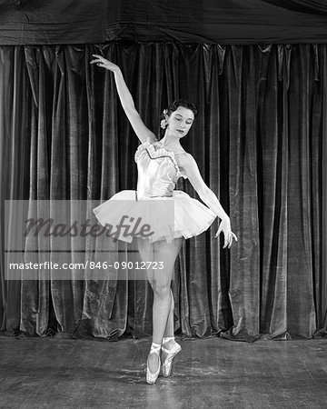 1950s BRUNETTE BALLERINA IN CLASSICAL POSE ON POINTE BEFORE CURTAIN ON STAGE
