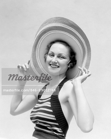 1930s PORTRAIT SMILING WOMAN IN STRAW HAT AND STRIPED HALTER TOP HOLDING THE HAT ON WITH HER HANDS SUN HAT LOOKING AT CAMERA