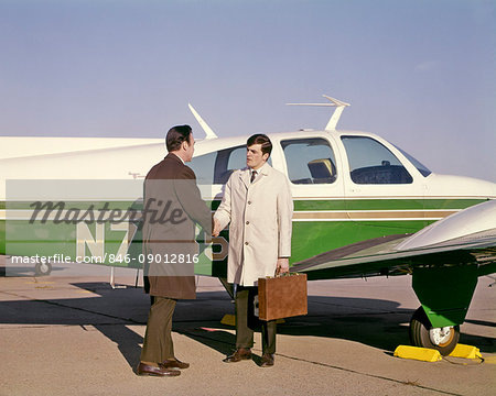 1960s TWO BUSINESS MEN SHAKING HANDS STANDING BESIDE SMALL PRIVATE AIRPLANE