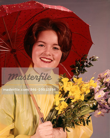 1960s SMILING BRUNETTE WOMAN WEARING YELLOW RAINCOAT HOLDING FLOWERS AND RED UMBRELLA LOOKING AT CAMERA