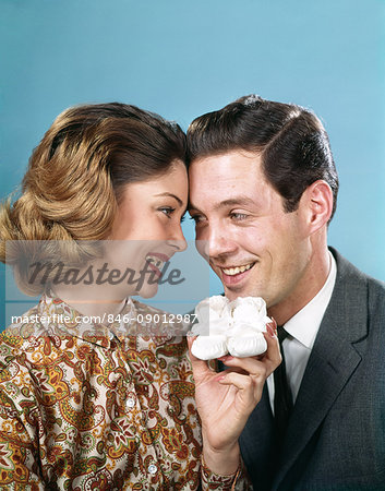 1960s SMILING COUPLE TOUCHING FOREHEADS LOOKING AT EACH OTHER HOLDING UP BABY SHOES 1960s SMILING COUPLE TOUCHING FOREHEADS LOOKING AT EACH OTHER HOLDING UP BABY SHOES