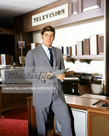 1960s SALESMAN STANDING IN TELEVISION SECTION OF DEPARTMENT STORE LOOKING AT CAMERA