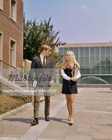 1960s 1970s YOUNG ADULT STUDENT COUPLE WALKING SIDE BY SIDE ON CAMPUS GIRL IN MINIDRESS BOY IN SUIT TIE