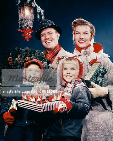 1950s FAMILY MAN WOMAN TWO KIDS HOLDING CHRISTMAS PRESENTS SMILING STANDING BENEATH LANTERN