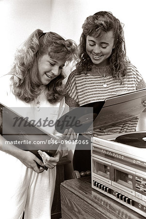 1980s 2 TEENAGE GIRLS READING VINYL RECORD ALBUM JACKET COVERS LISTENING TO LONG PLAYING PHONOGRAPH PLAYER