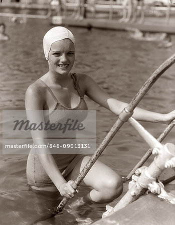 1930s SMILING YOUNG WOMAN WEARING ONE PIECE BATHING SUIT & CAP CLIMBING OUT OF POOL LOOKING AT CAMERA ON VACATION IN FLORIDA USA