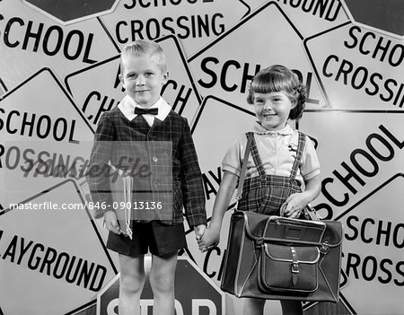 1950s MONTAGE OF BOY & GIRL IN PLAID JACKET & SKIRT HOLDING HANDS LOOKING AT CAMERA SUPERIMPOSED OVER SCHOOL CROSSING SIGNS