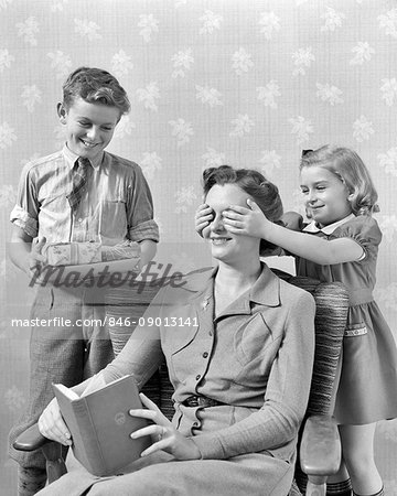 1930s 1940s LITTLE GIRL HAND OVER MOTHER EYES BOY WITH WRAPPED PRESENTS SURPISE CHRISTMAS OR MOTHER'S DAY