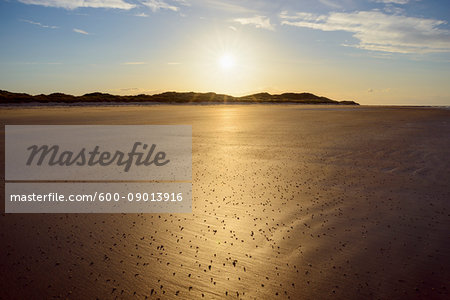 Sun reflecting on the sandy beach at low tide with the North Sea at sunrise at Bamburgh in Northumberland, England, United Kingdom Sun reflecting on the sandy beach at low tide with the North Sea at sunrise at Bamburgh in Northumberland, England, United Kingdom