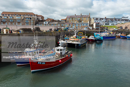 Harbour with fishing boats docked at seawall in the village of Seahouses in Northumberland, England, United Kingdom