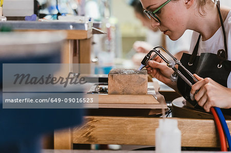 Female jeweller using blow torch at workbench