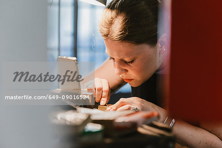 Female jeweller engraving metal at workbench