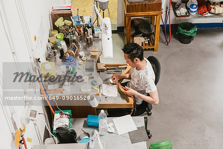 High angle view of male jeweller using blow torch at workbench