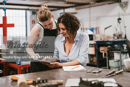 Two female jewellers looking at digital tablet at workbench