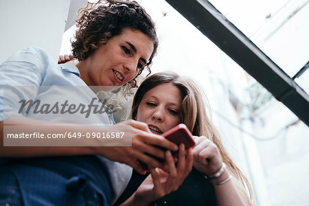 Low angle view of two female jewellers looking a smartphone in jewellery workshop