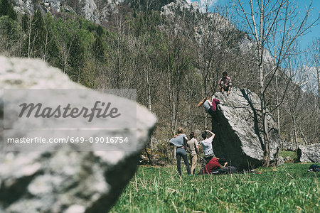 Adult bouldering friends climbing boulder, Lombardy, Italy