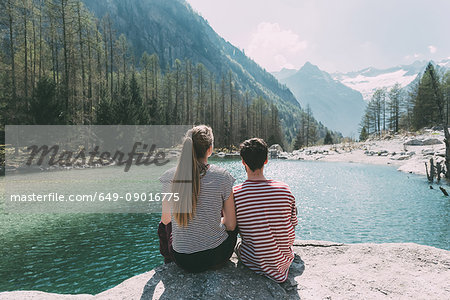 Rear view of young hiking couple looking out at mountain lake, Lombardy, Italy