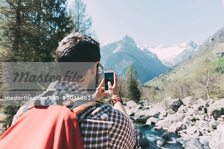 Rear view of male hiker photographing mountain river, Lombardy, Italy