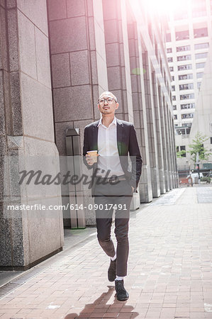 Cool businessman with takeaway coffee strolling along sidewalk, New York, USA