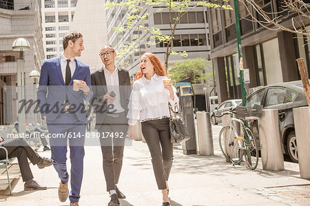 Young businesswoman and businessmen with takeaway coffee strolling along sidewalk, New York, USA