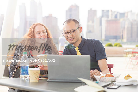 Businessman and woman using laptop at waterfront cafe table, New York, USA