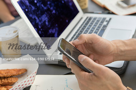 Hand of businessman holding smartphone at cafe table