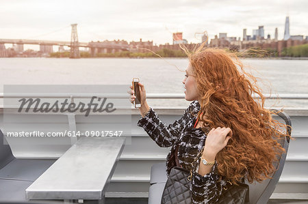 Young businesswoman on passenger ferry deck taking smartphone selfie