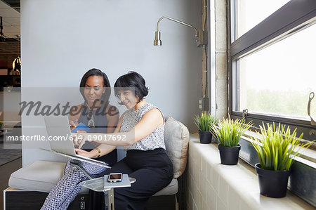 Two women sitting, working on laptop, on laptop stand