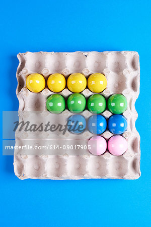 Overhead view of multi- coloured painted eggs in tray on blue background