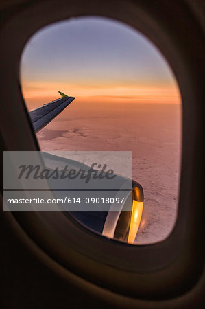 Sunset cloudscape and airplane wing through airplane window