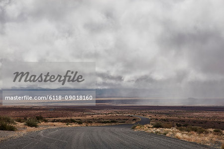 Road running through grassland under storm clouds.