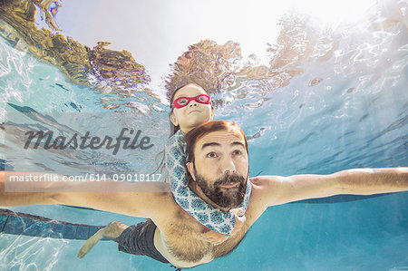 Underwater view of mature man swimming with daughter on piggy back