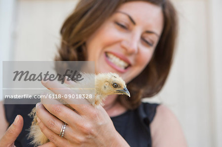 A woman holding a small fluffy chick, a baby bird in her two hands.