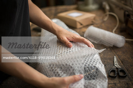 A woman wrapping an item in bubble wrap, a parcel being prepared for despatch.