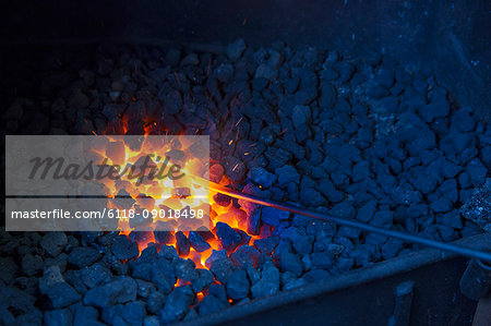 A glowing metal rod in the hot coals in a blacksmith's forge.
