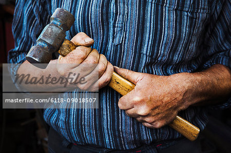 Close up of blacksmith's hands gripping a large hammer.