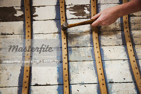 Close up of person in a boat-builder's workshop, working on a wooden boat hull.