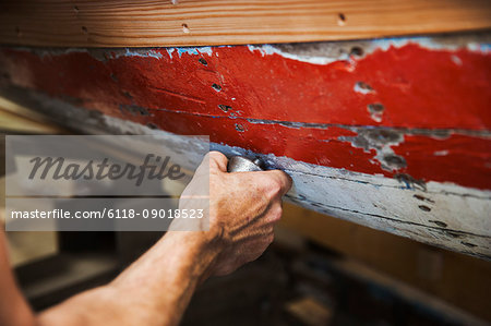 Close up of person in a boat-builder's workshop, working on a wooden boat hull.