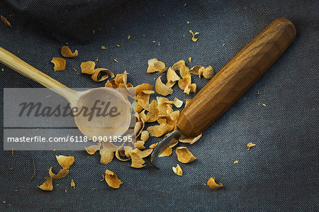 Close up of a handmade handcarved wooden spoon with round bowl end, a sharp carver's knife and wood shavings.