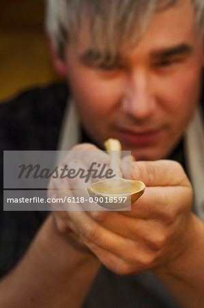 A craftsman holding and inspecting a handcrafted hand made wooden spoon with a long slender handle and round polished bowl.