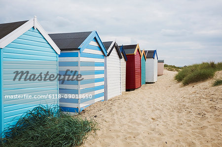 Row of colourful painted beach huts on a sandy beach under a cloudy sky.